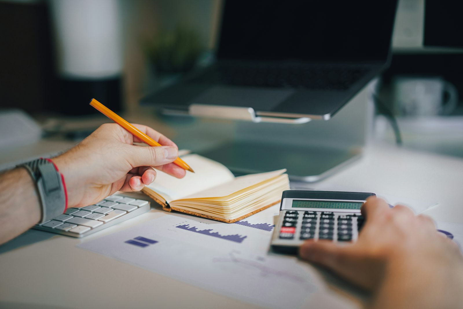 A person working through numbers at a desk with a calculator and notebook